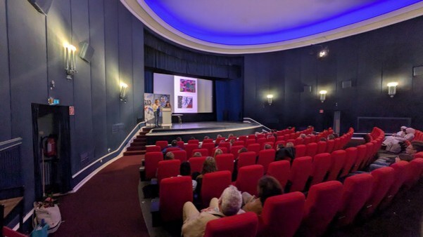 Kunstlehrerin Nadine Knoll von der Gemeinschaftsschule Lauenburgische Seen und Volkshochschulleiterin Silvia Tessmer präsentieren die Bilder des Schul-Kunstprojektes "WIR und DIE ANDEREN" auf der Bühne des Burgtheaters. © Stadt Ratzeburg